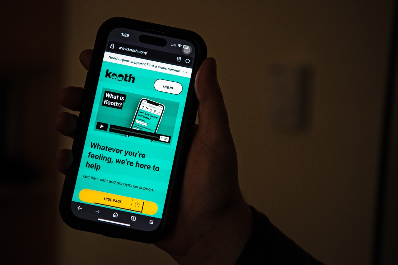 A photo of a hand holding up a phone with the Kooth website opened.