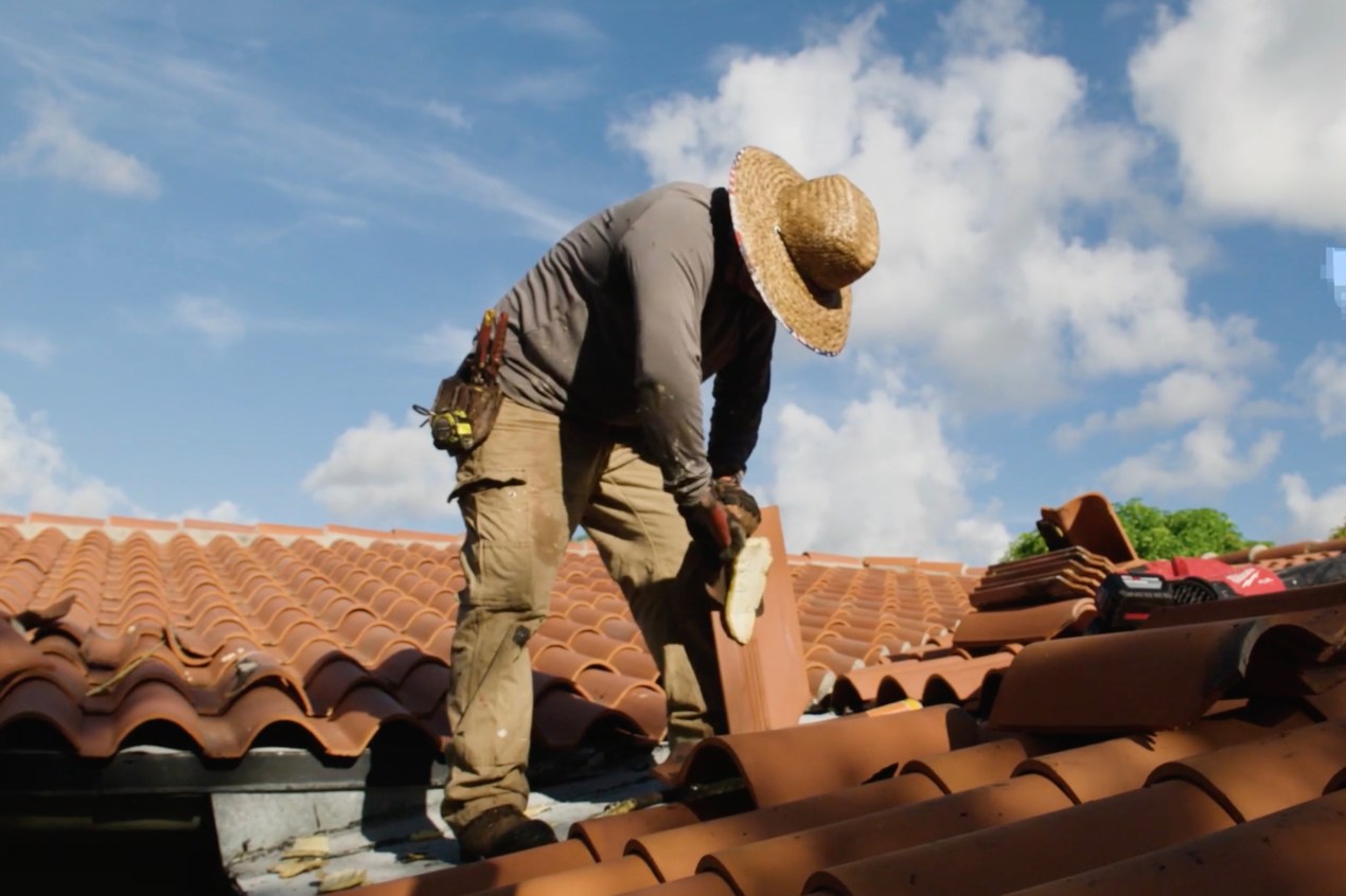 A photo of a roofer working on a roof on a sunny day. His hat is covering his face.