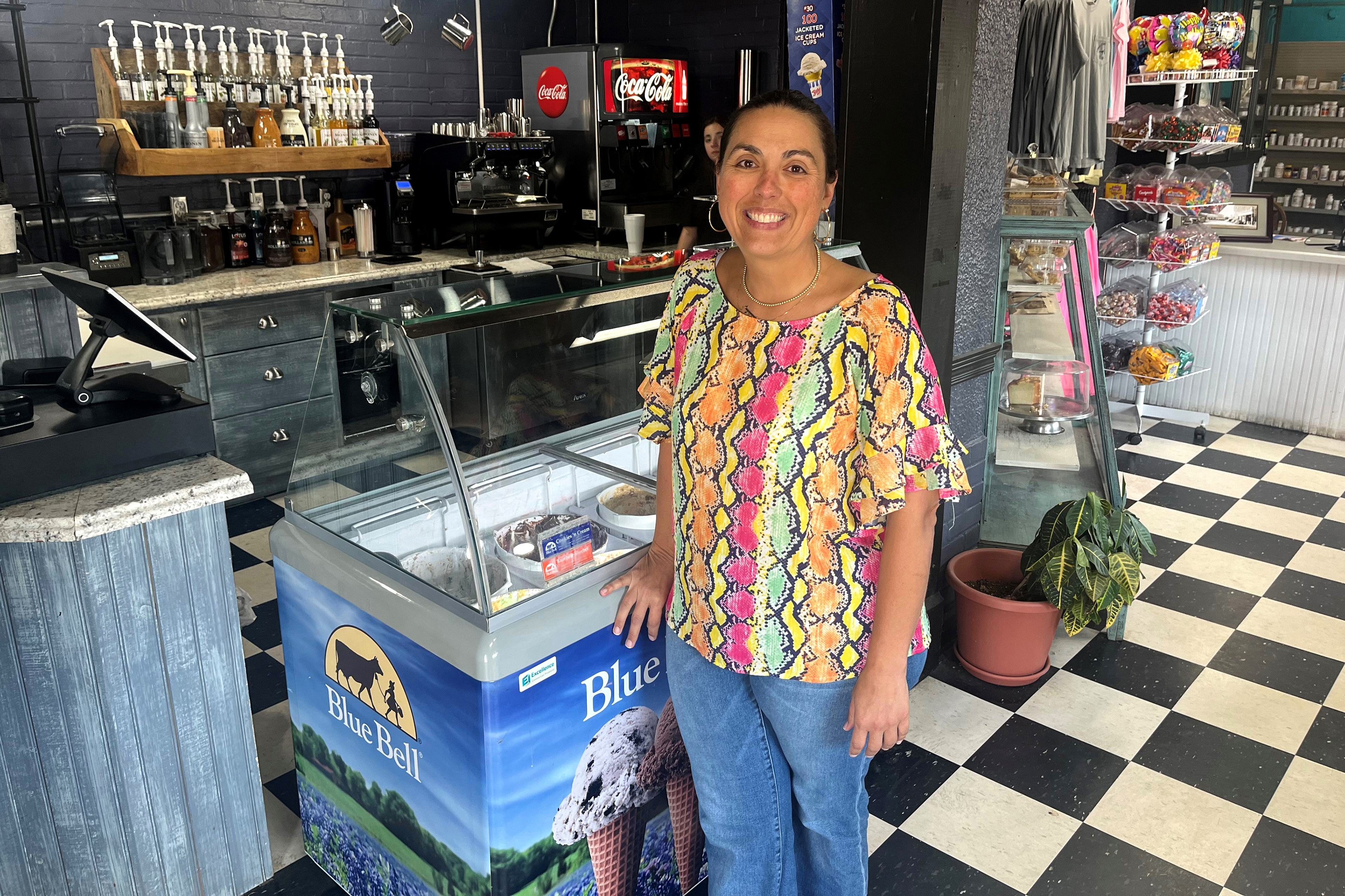 Nikki Bryant, a woman with brown hair pulled back in a ponytail, smiles for a photograph inside her family pharmacy.