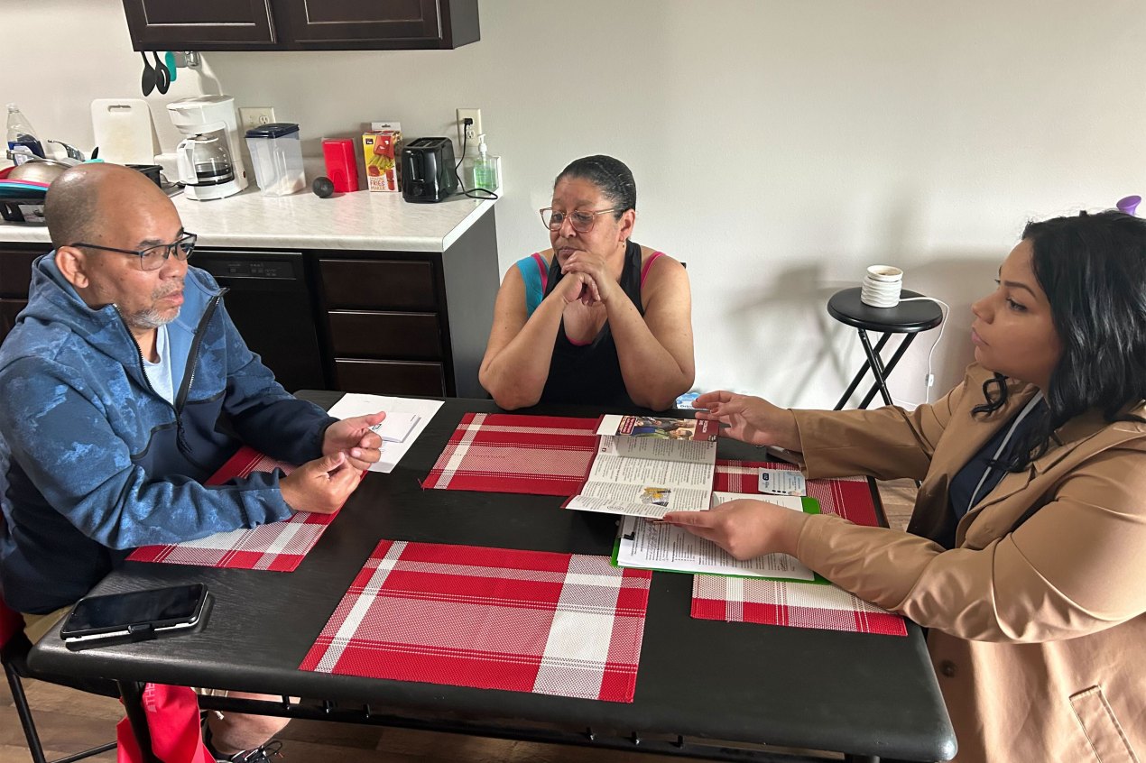 A photo of two people sitting across a table with a community health worker.