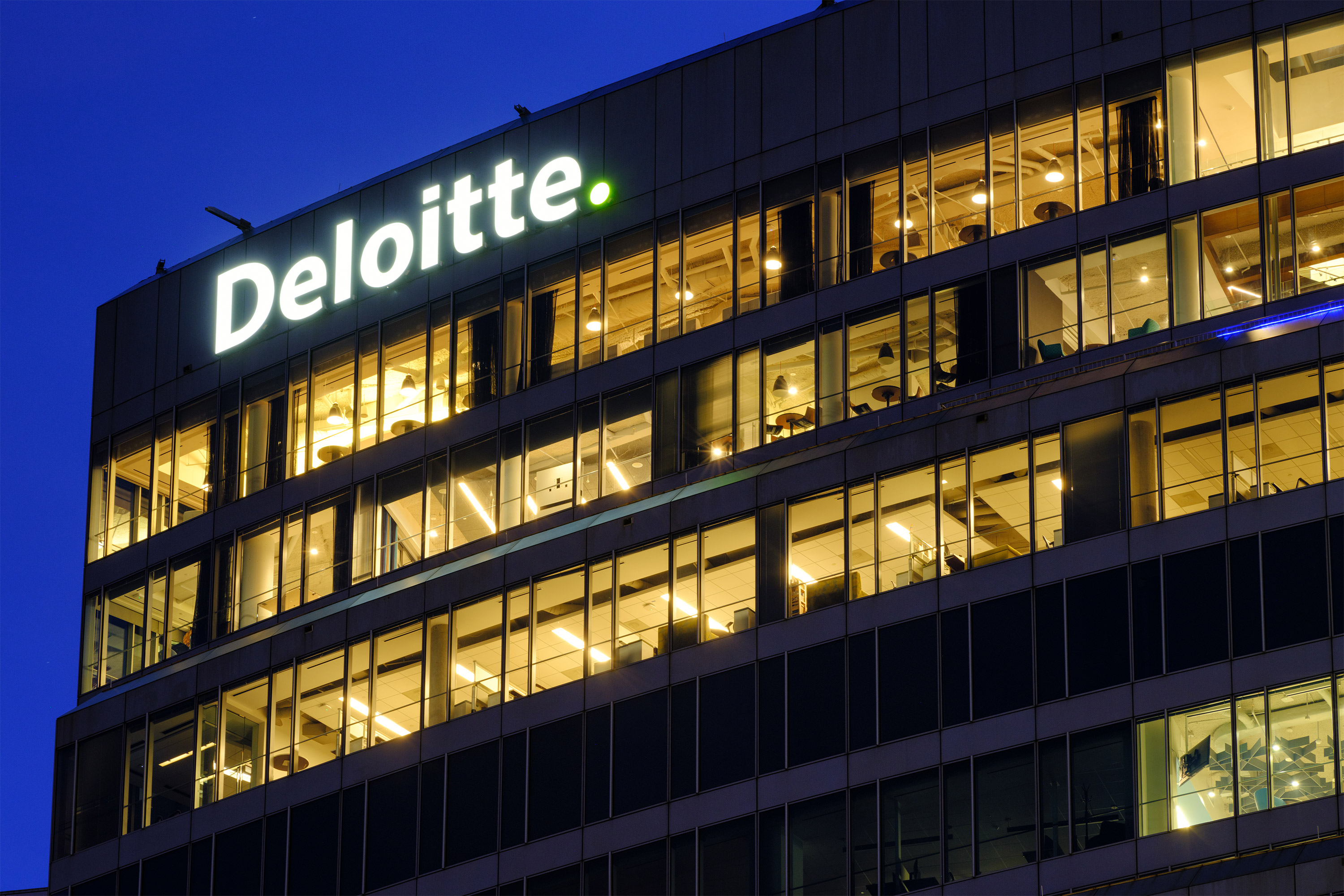 A photo of a Deloitte office building taken at dusk, with the company's logo on the building lit.