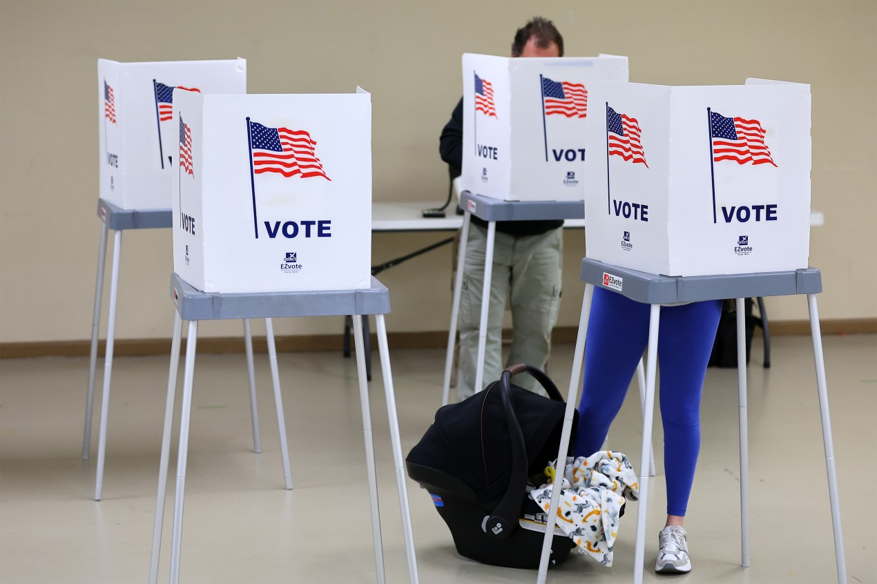 A photo of two voters — a man in the back and a woman with a baby carrier in the front.