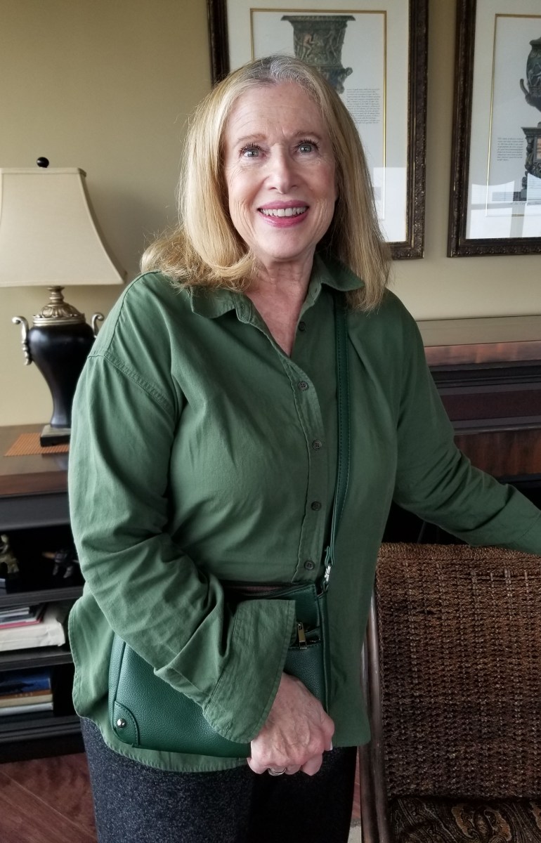 Jobie Stern, a senior woman with blonde hair, stands in a room and wears a green jacket.