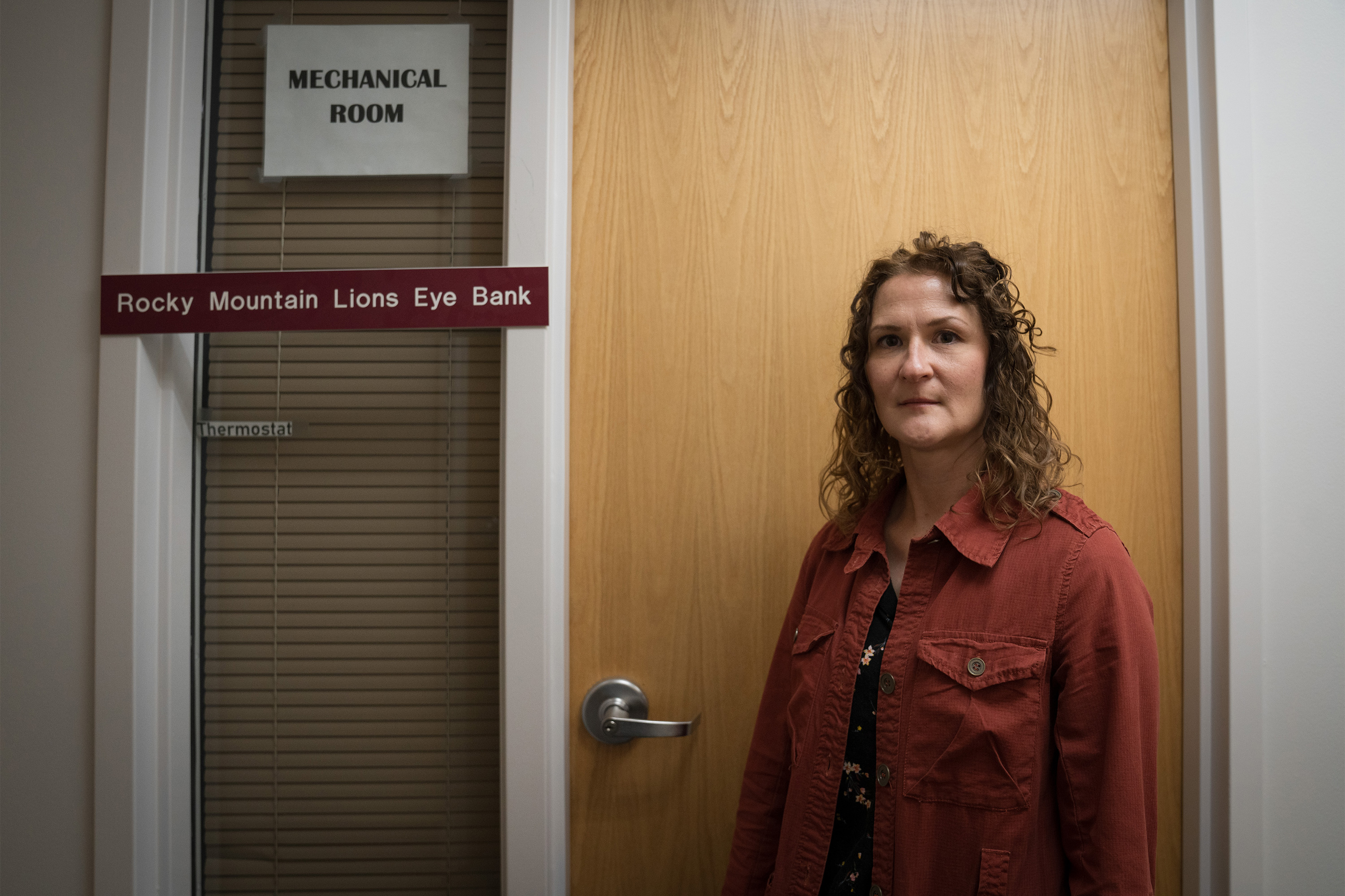 A photo of a woman standing by a door with a Rocky Mountain Lions Eye Bank sign next to it.