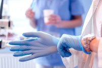 A close up photo of a doctor's hands putting on blue sterilized surgical gloves in a medical setting.