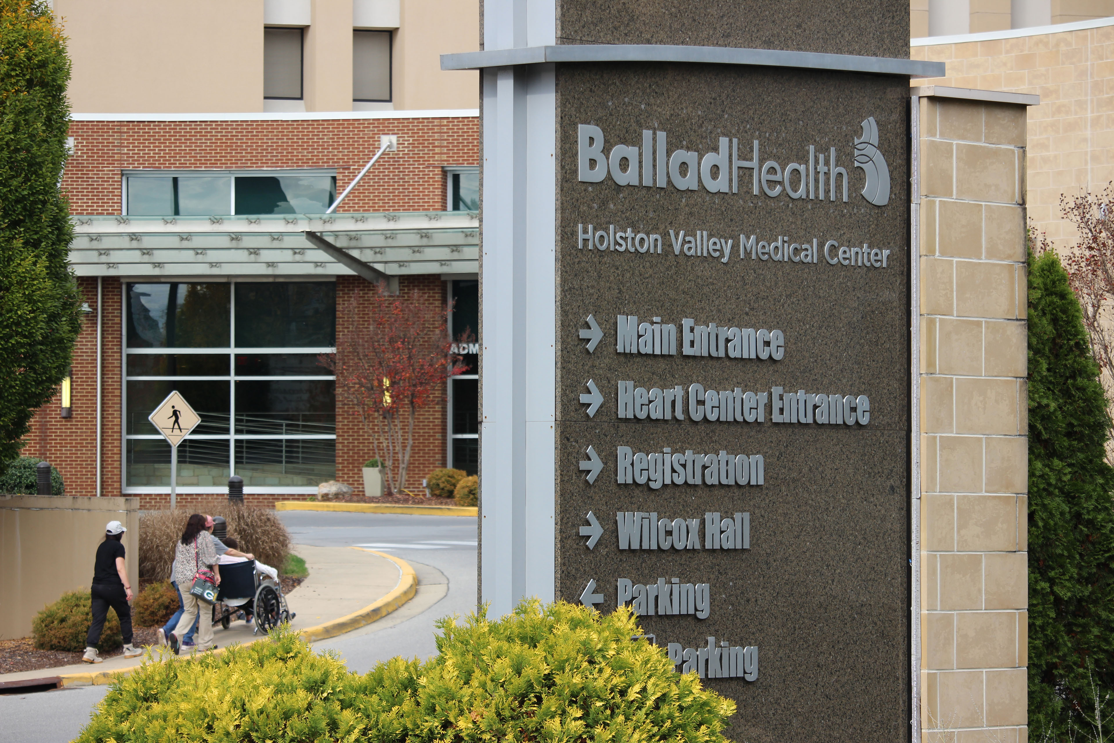 The entrance to Holston Valley Medical Center, a part of the Ballad Health hospital system. A sign that says, "Ballad Health" with directional arrows to different departments is in the foreground.