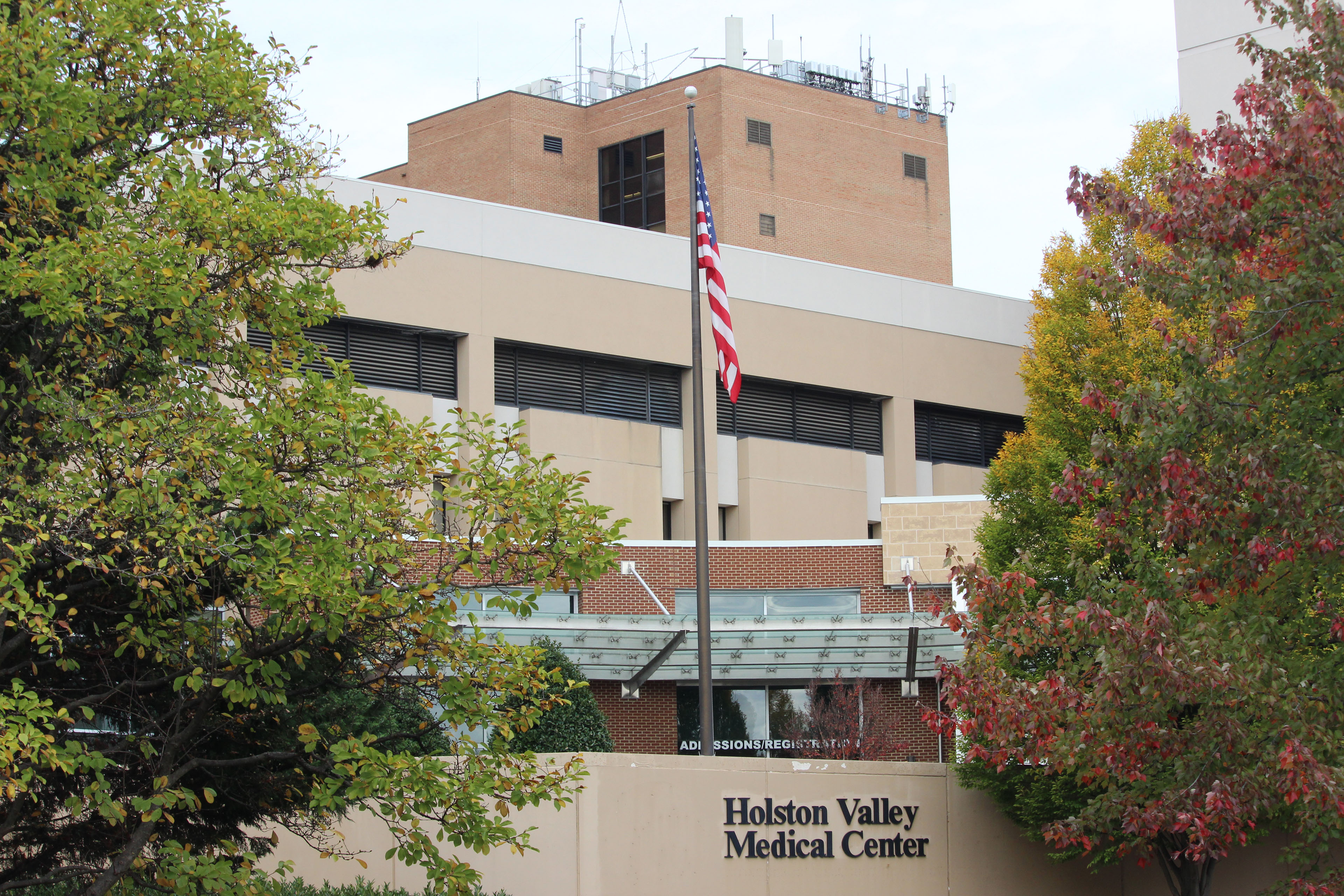 An exterior photograph of the Holston Valley Medical Center. An American flag on a flagpole stands in the center.