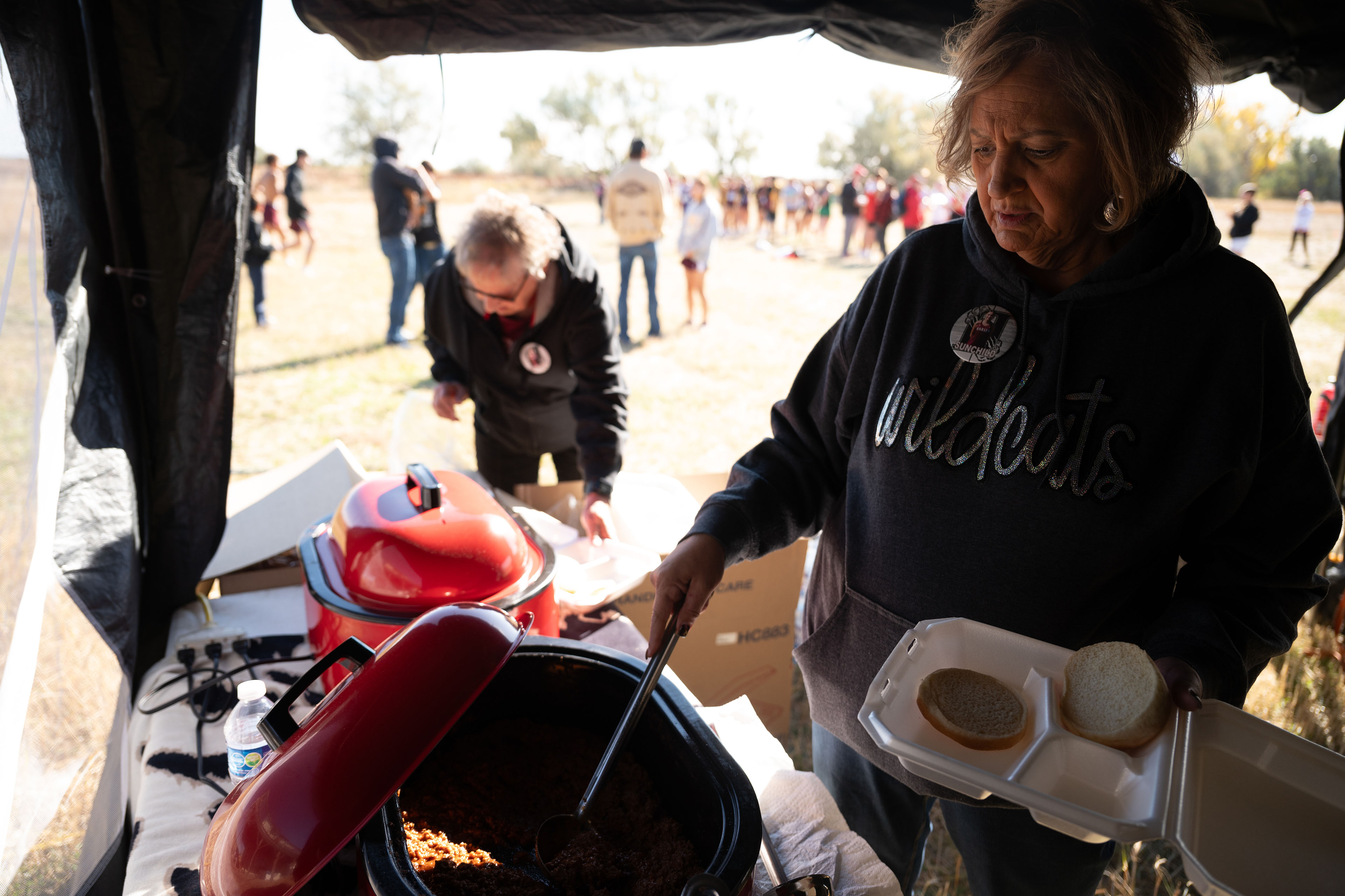 A woman is using tongs to flip food on a circular grill.