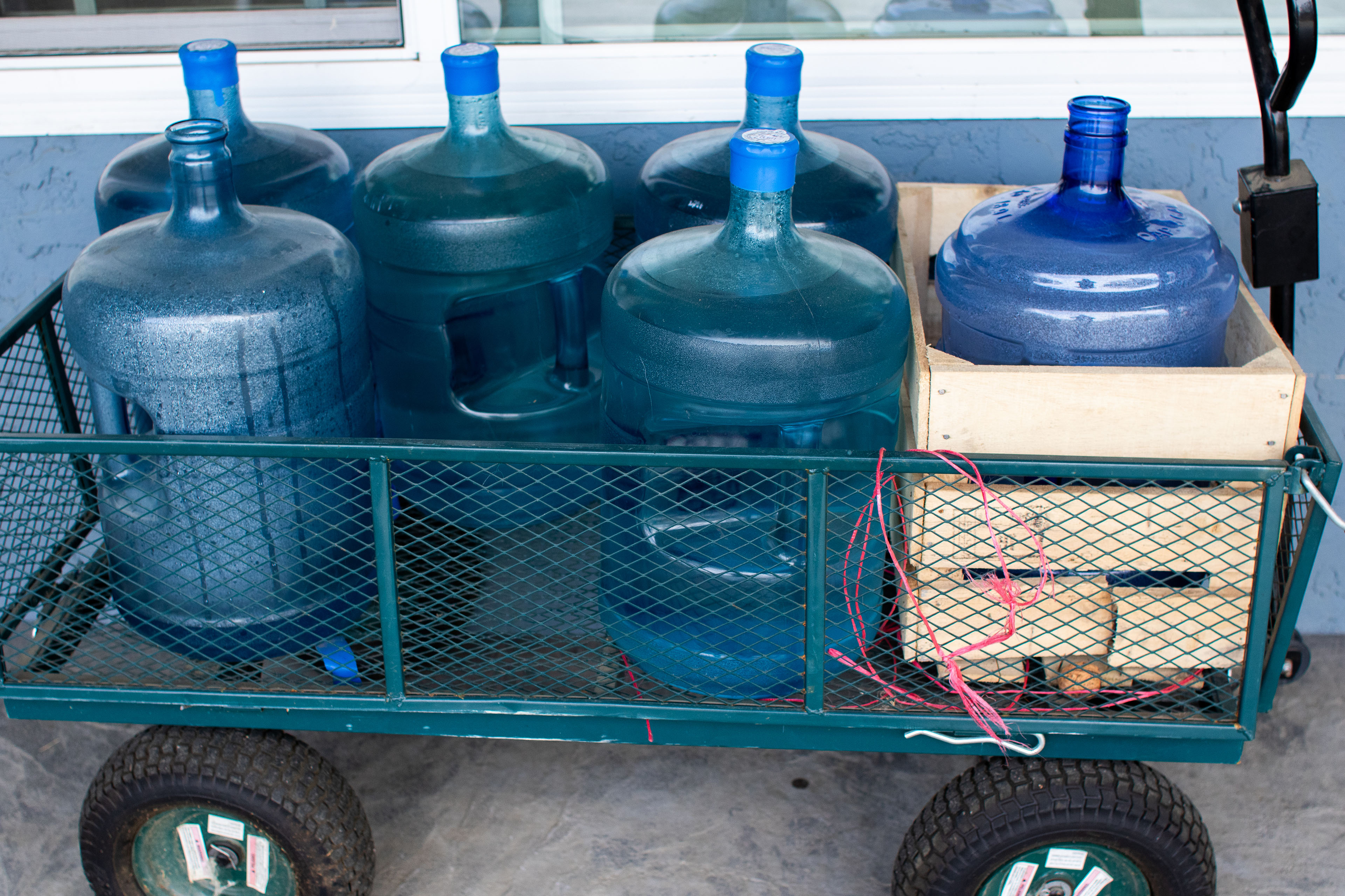 A photograph of large, blue plastic water-cooler jugs in a green metal cart.