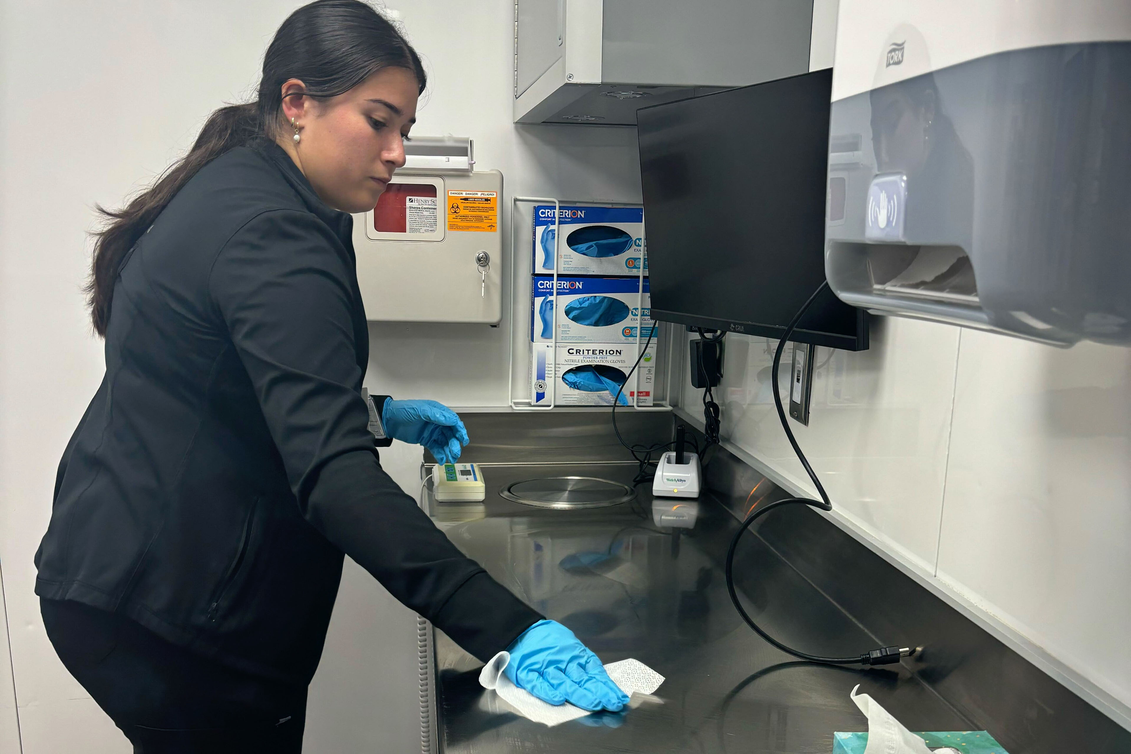 A woman is shown disinfecting a countertop in a doctor's office.