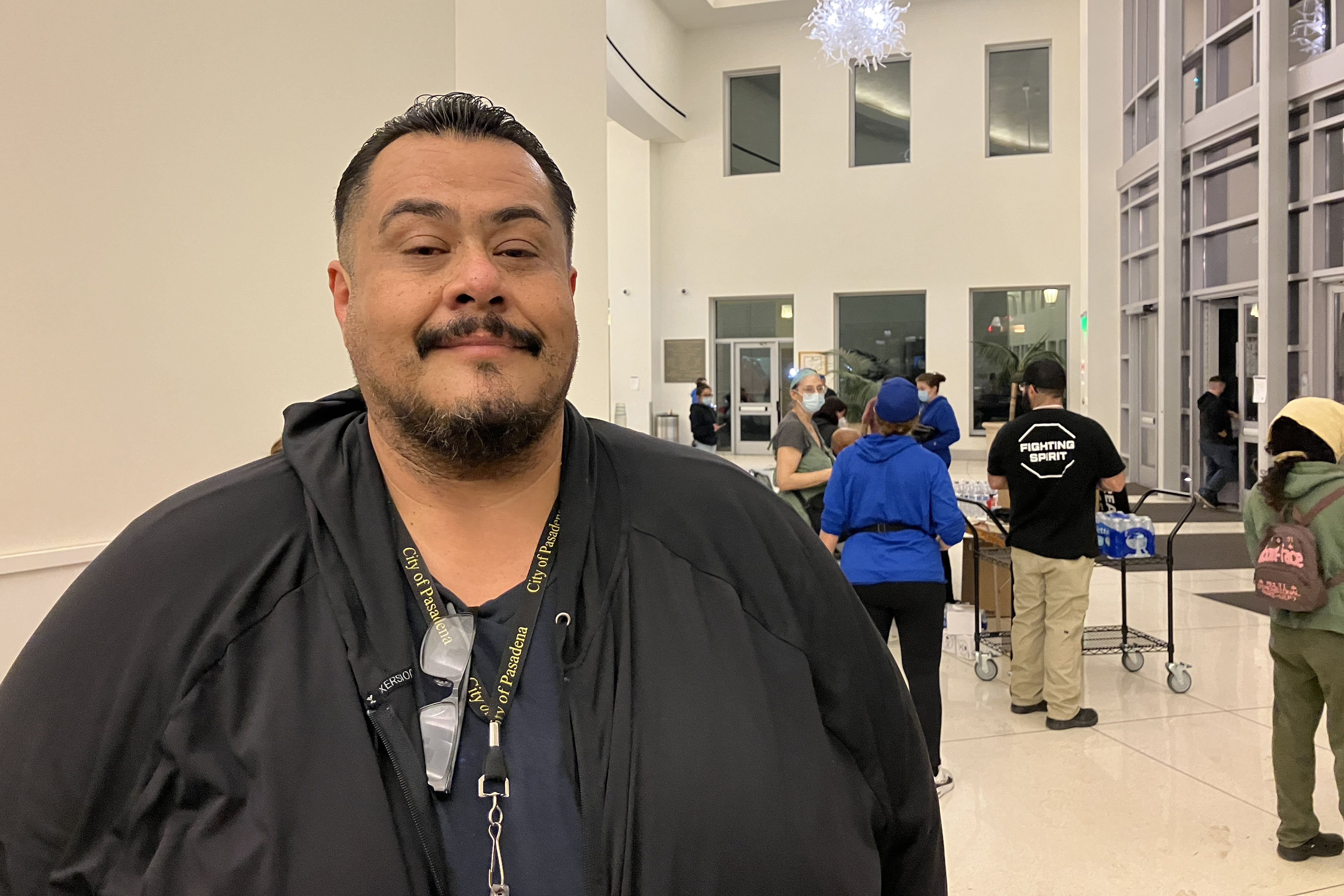 A man wearing a navy shirt and a black sweatshirt poses for a photo inside a convention center