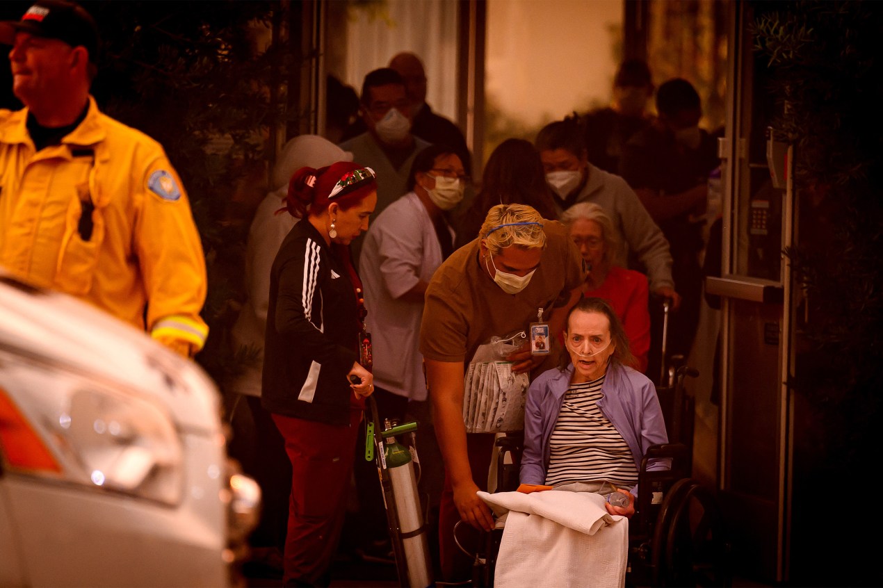 A photo of nursing home staff wheeling out an elderly woman as the facility is evacuated due to a wildfire.