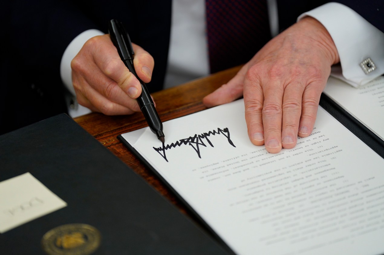 A photo of President Trump signing his name with a marker onto an executive order.