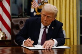 President Donald Trump signs behind a desk in the Oval Office and signs a document.