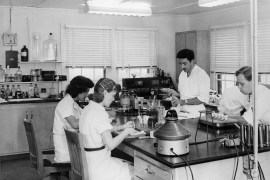 A black and white photograph from 1952 that shows four lab technicians, two men and two women, working at a table with science equipment.