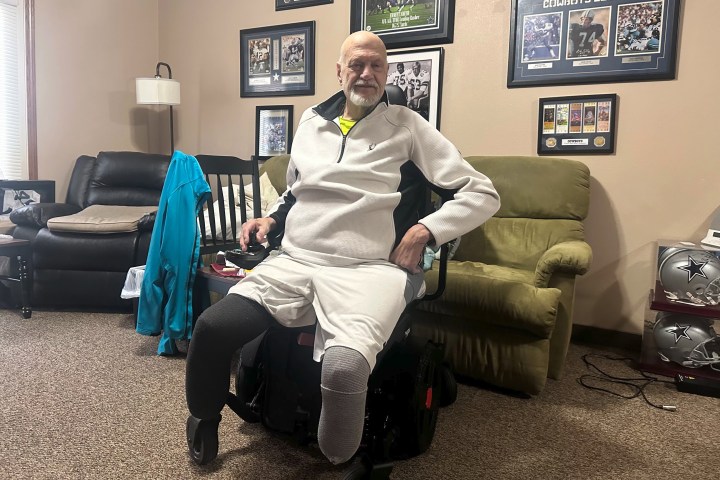 A photo of a man inside an apartment, seated in a wheelchair.