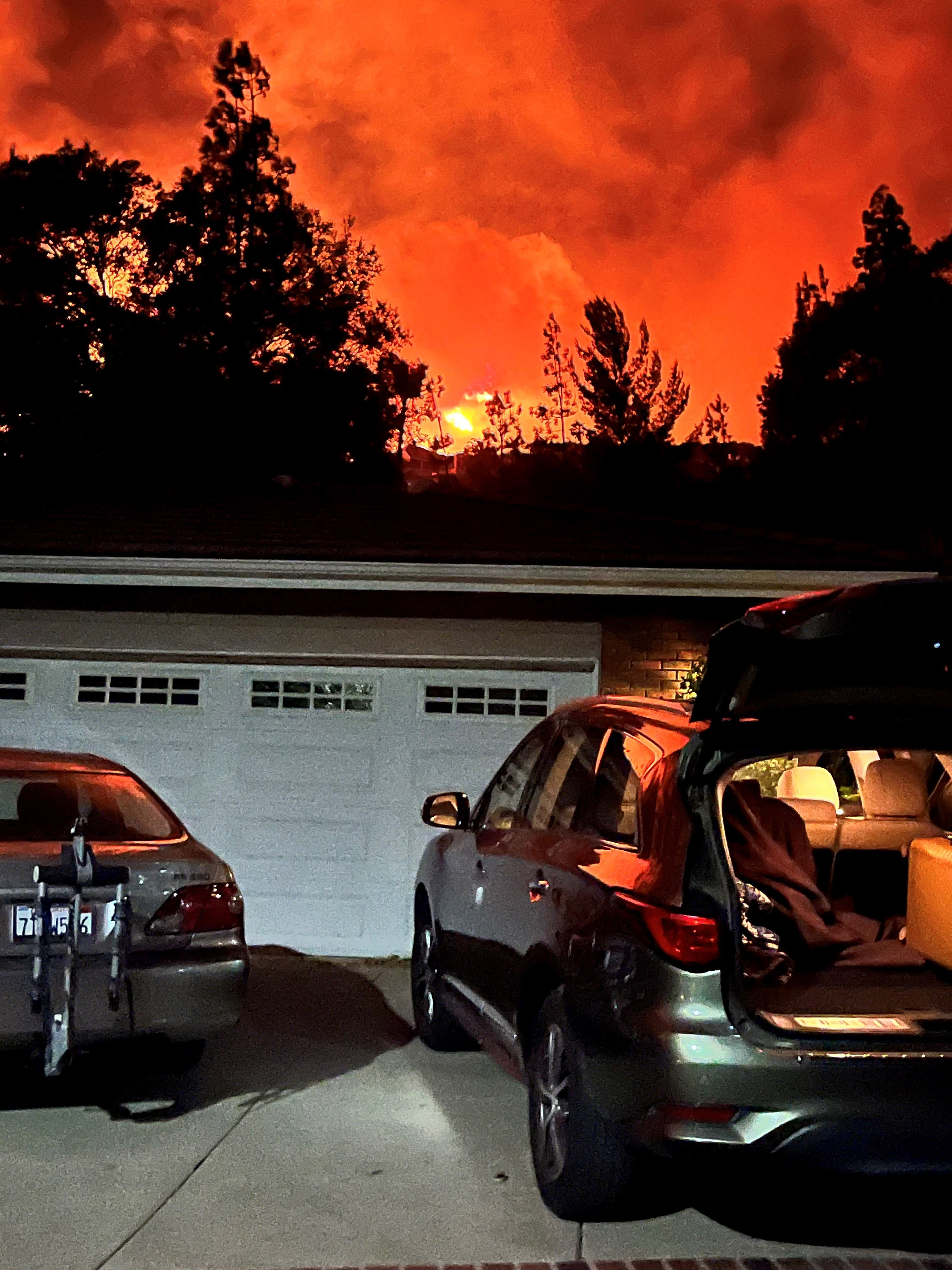 A photo showing a car in front of a home garage. The sky in the background is bright orange, set ablaze from wildfires.