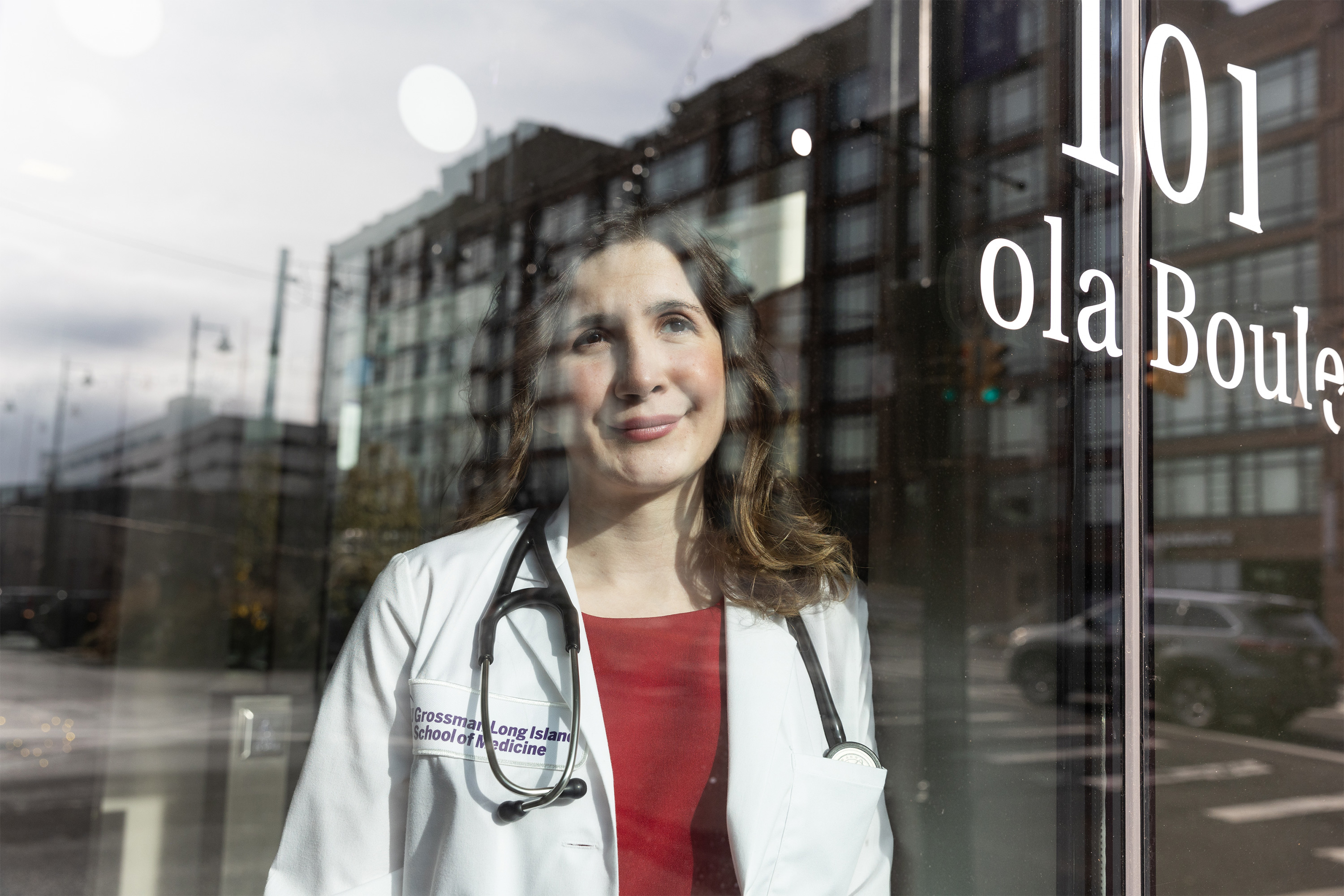 A photo of Julia Lo Cascio shot with her standing behind a relective glass door. A view of the building across the street is reflected over her face.