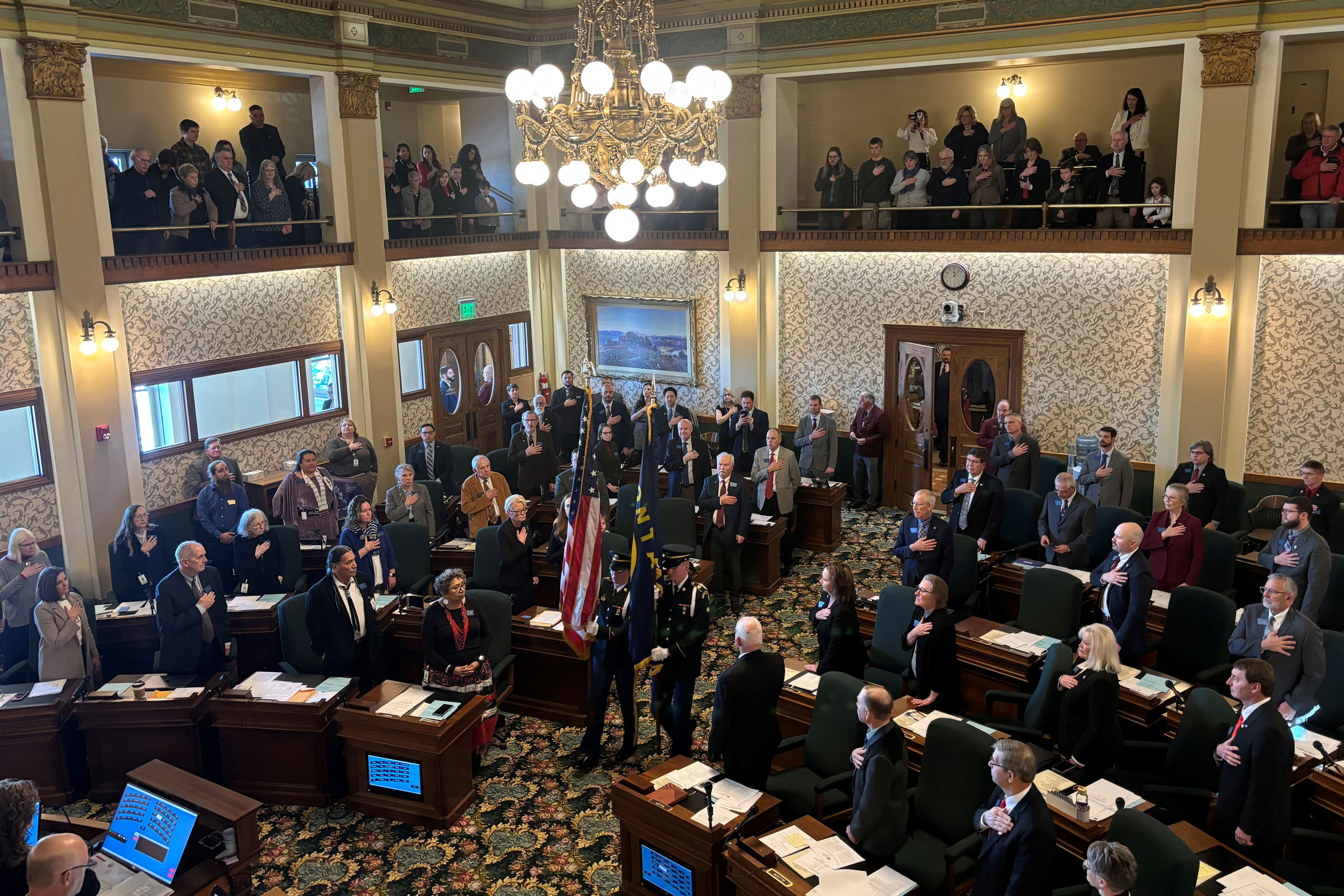 A photo of Montana state senators standing as a two flagbearers carry a U.S. and Montana flag into the room.