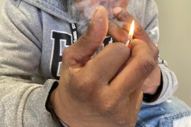 A close-up image of an unidentifiable man's hands as he uses a lighter and smokes.