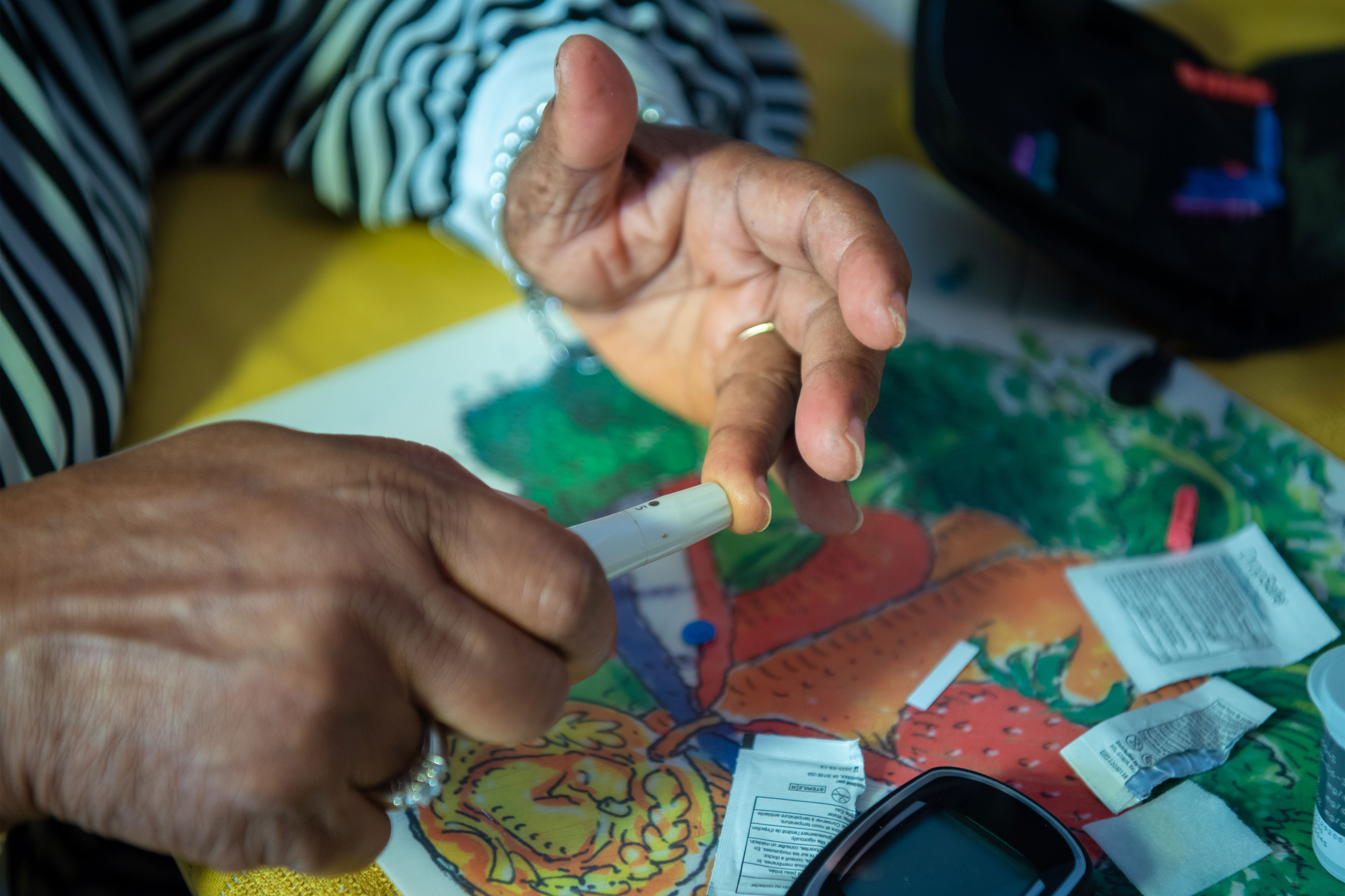 A close-up image of a woman's hands as she holds a lancing device to the ring finger of her left hand.