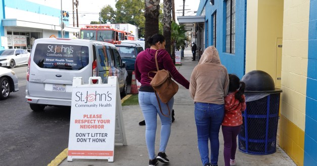 A photo of a woman walking with two kids on the sidewalk by a health clinic in California.