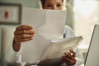 A photograph of a woman holding up a piece of paper. Her face is obstructed from view.