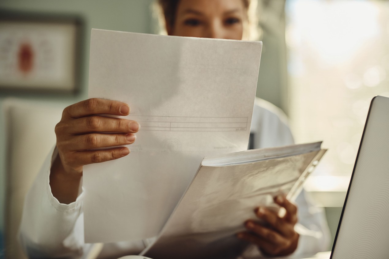 A photograph of a woman holding up a piece of paper. Her face is obstructed from view.