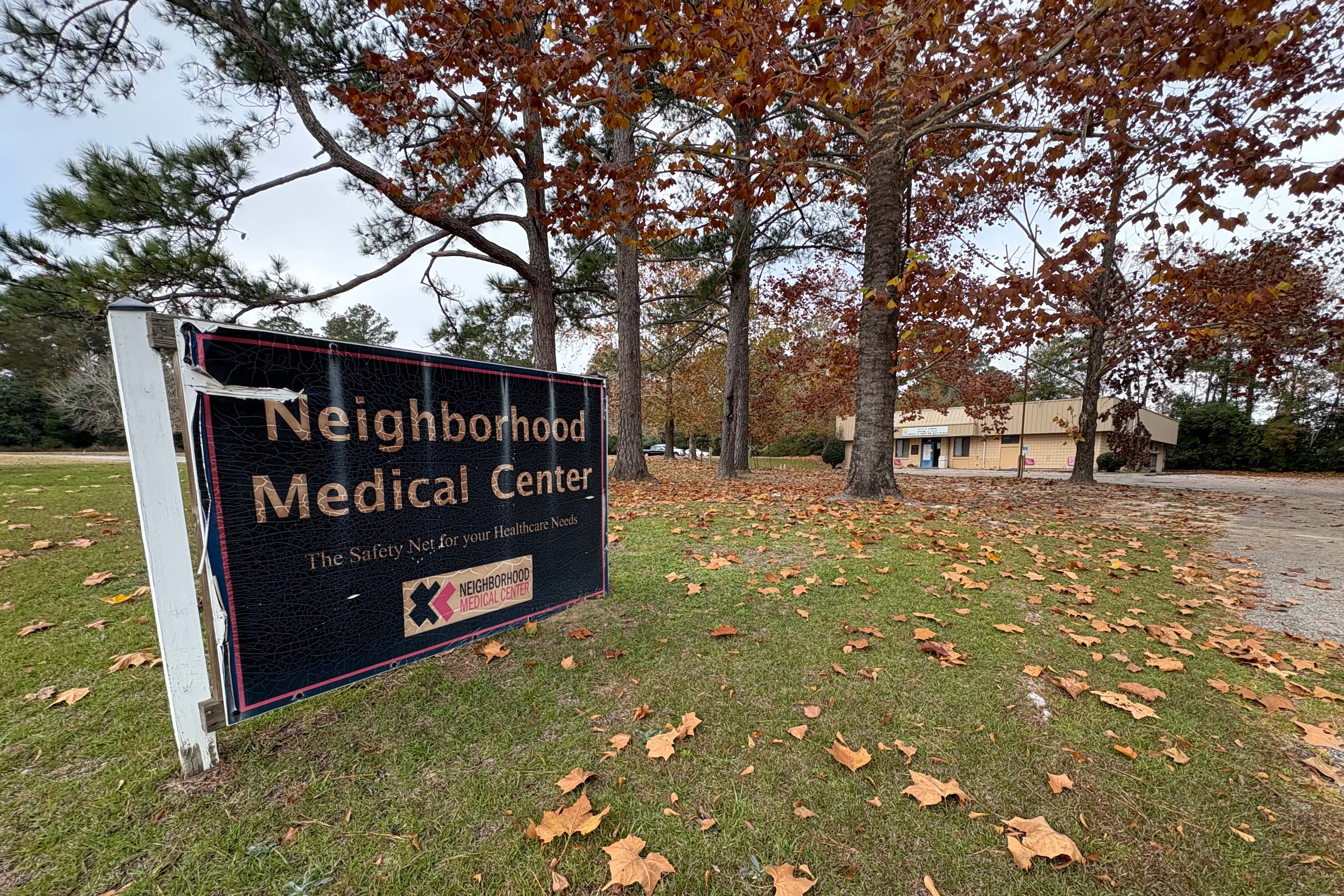 An outdoor entrance sign, which has become warn and distressed from weather and age, reads "Neighborhood Medical Center."