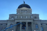 A photo of Montana's capitol with a few inches of snow. A construction worker in the foreground works on the building from a cherry-picker basket.