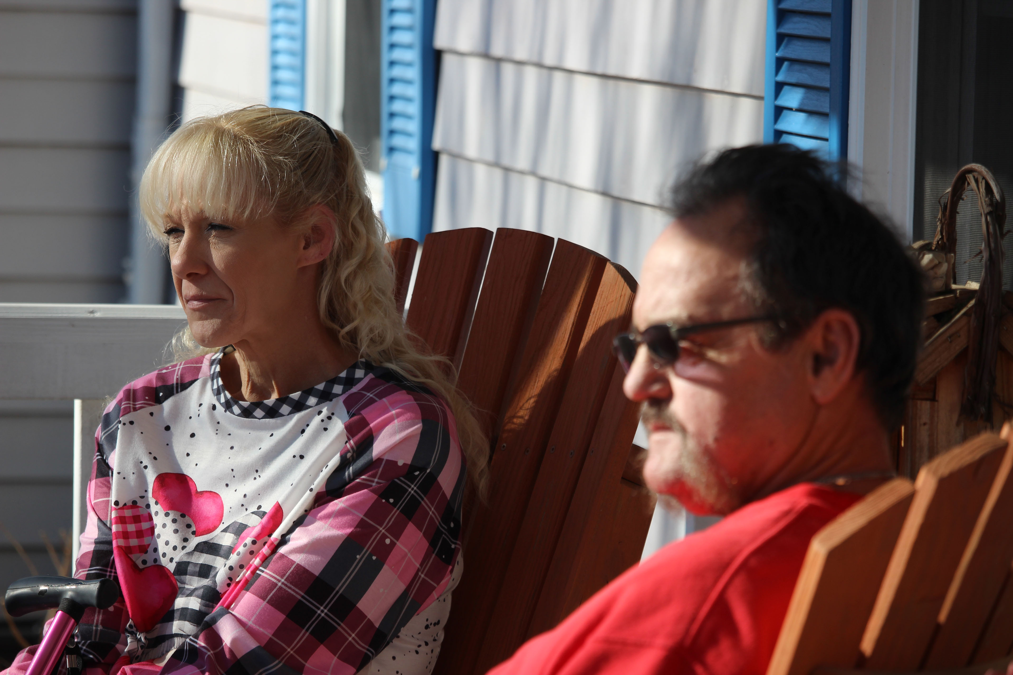 A tightly cropped photo of a woman and man sitting on their porch on wooden chairs.