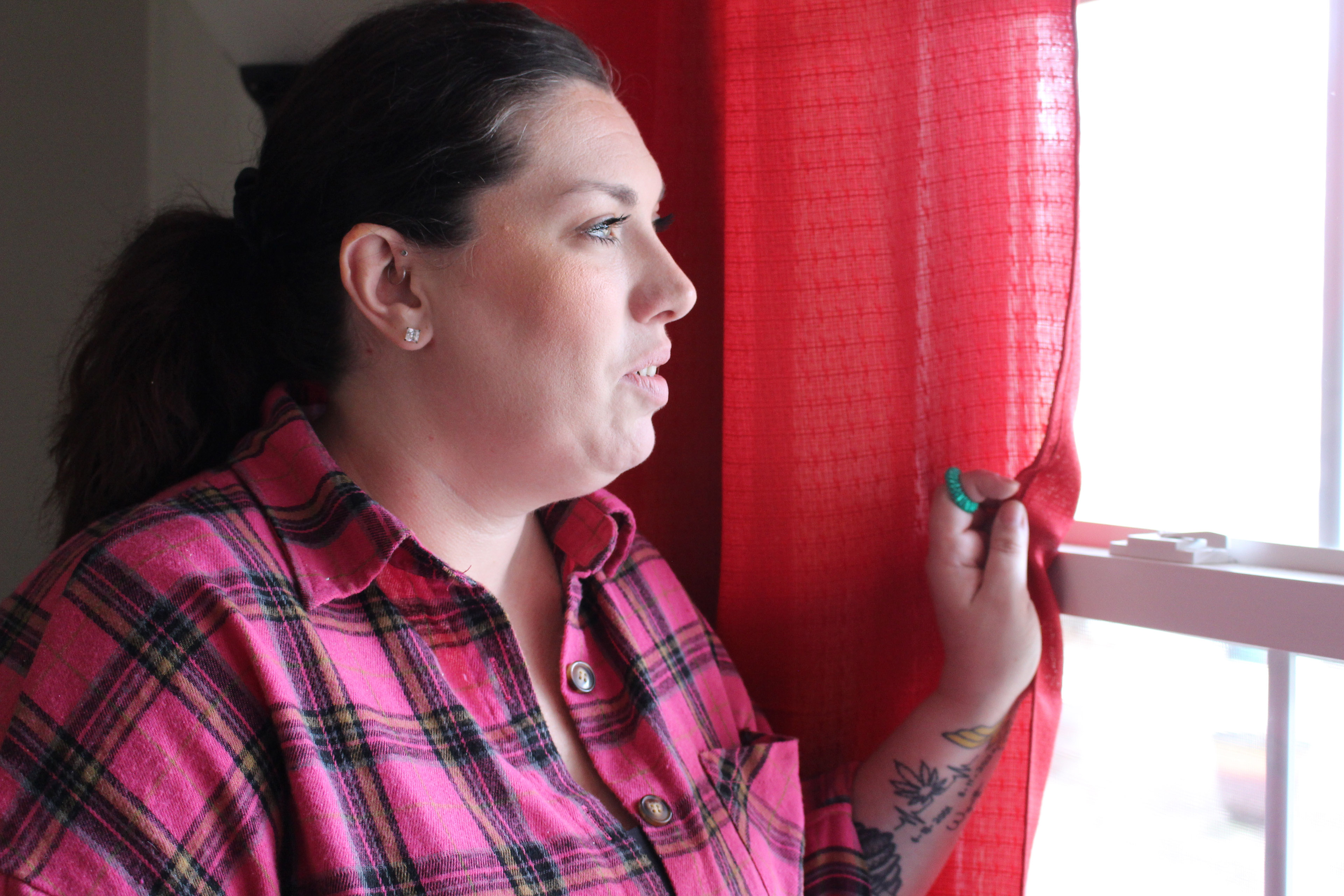 A woman in a pink plaid shirt looks out a window