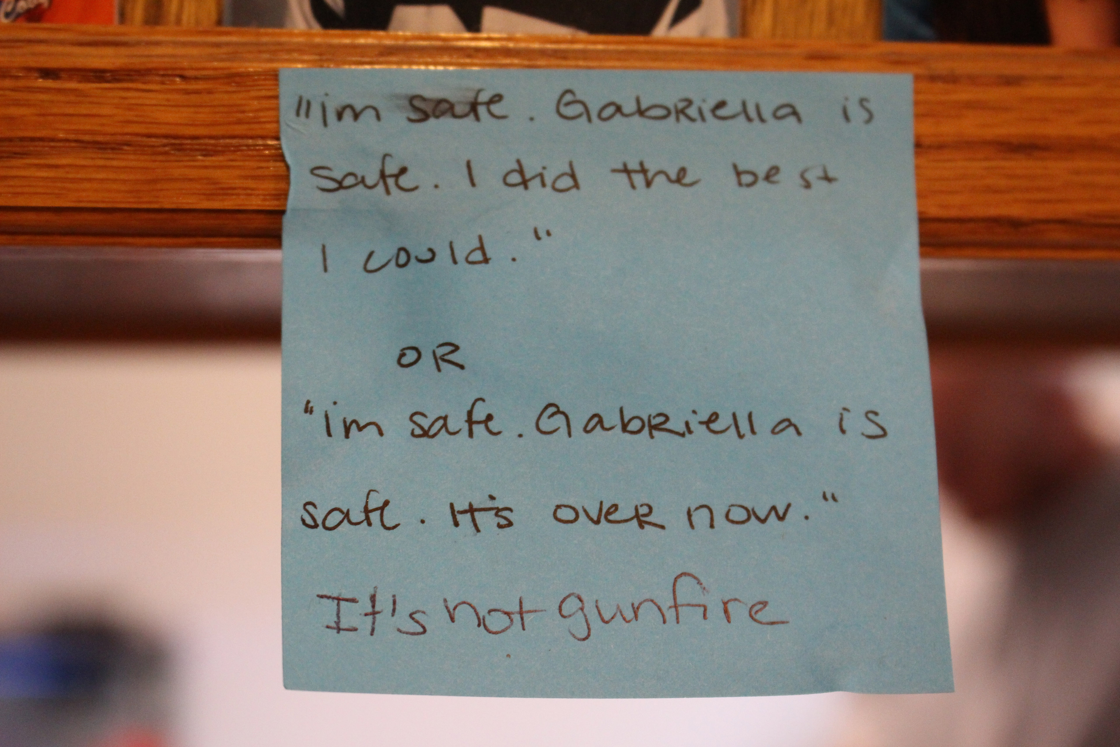 A blue Post-it note with handwriting hangs from a wooden cabinet