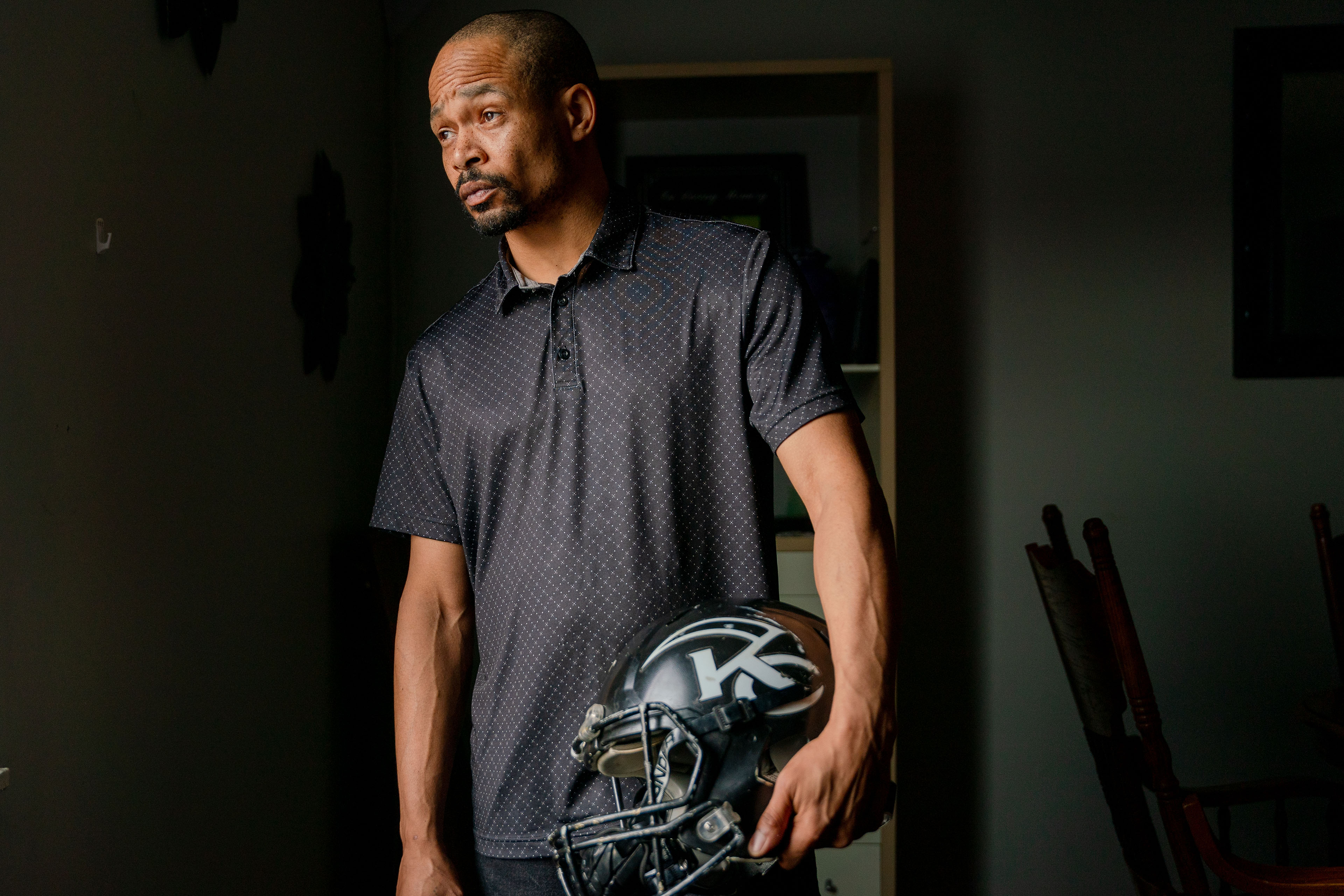 A man in a navy collared shirt poses for a photo holding a football helmet