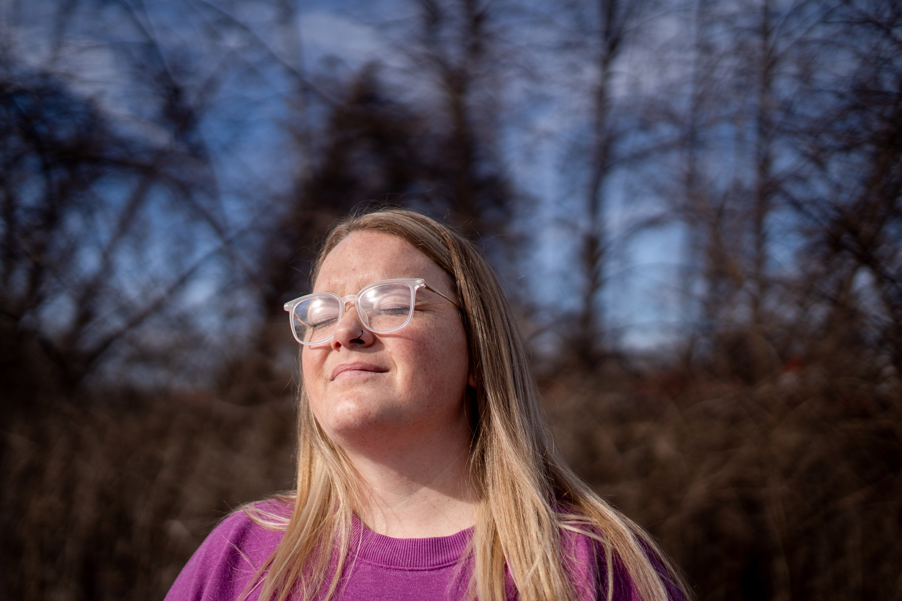 A woman with blonde hair and glasses closes her eyes as she faces the sun