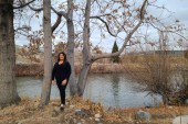 A woman stands out in a wooded area by a pond in autumn.