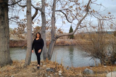 A woman stands out in a wooded area by a pond in autumn.