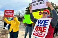 A photo of protesters holding signs outside that read, "Stop the billionaire takeover," "Stop Elon now. Nobody elected Elon," "Workers over billionaires," and "We are one. Respect our rights."