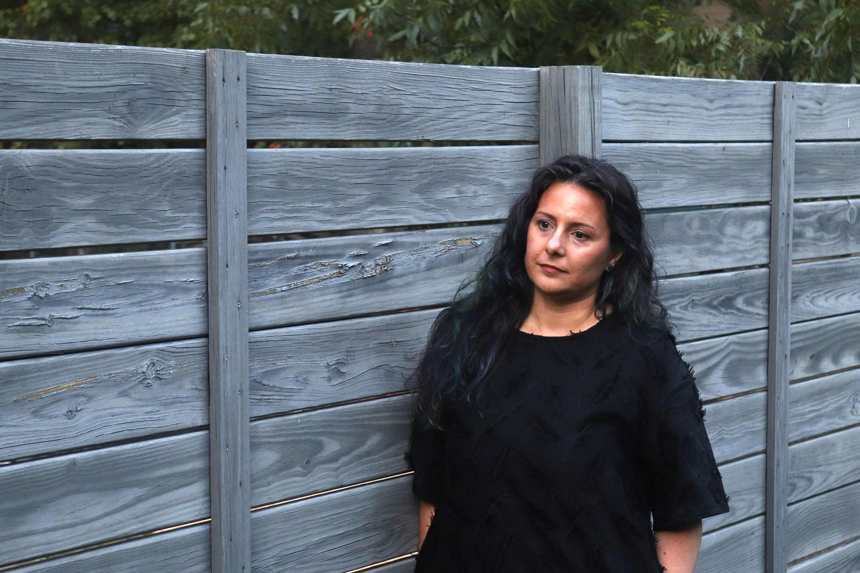 A photo of a woman standing outside for a portrait next to a fence.