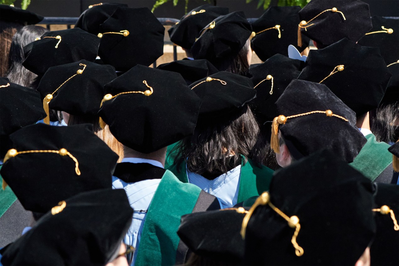 A photo of a crowd of medical school graduates donned in tams and gowns standing during a graduation ceremony.