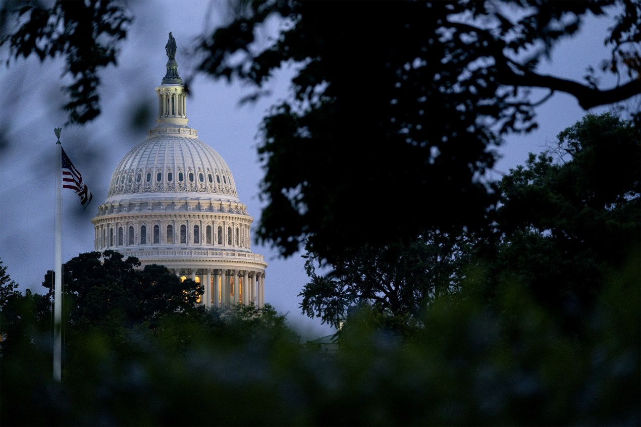 A photo of the U.S. Capitol from afar, framed by trees.