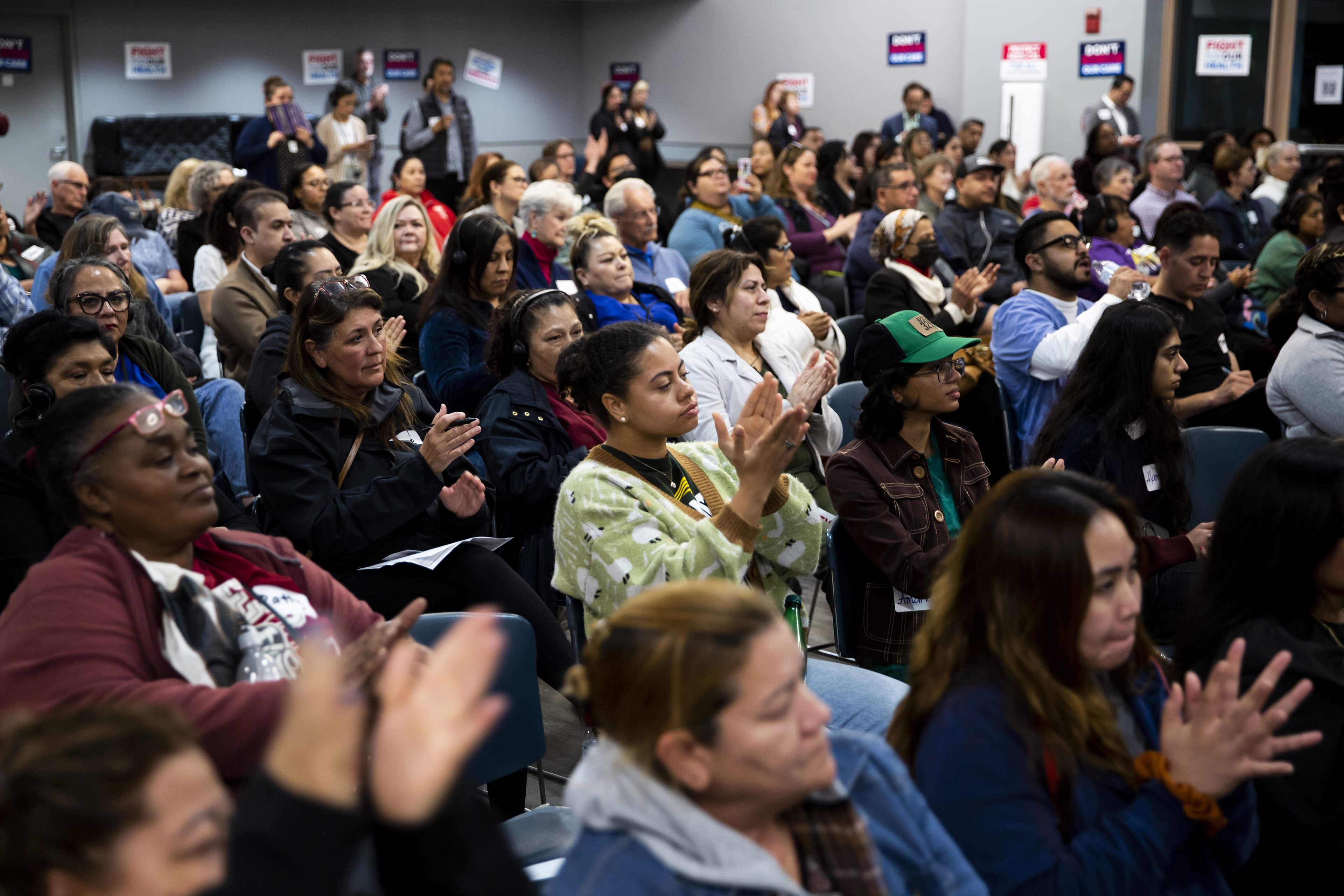 Participants sitting in a crowded play in a town hall event applaud.