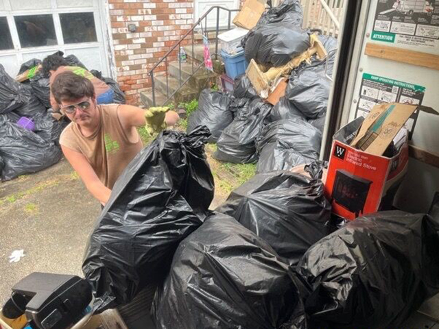 A photo of a man lifting a trash bag filled with clutter into a box truck.