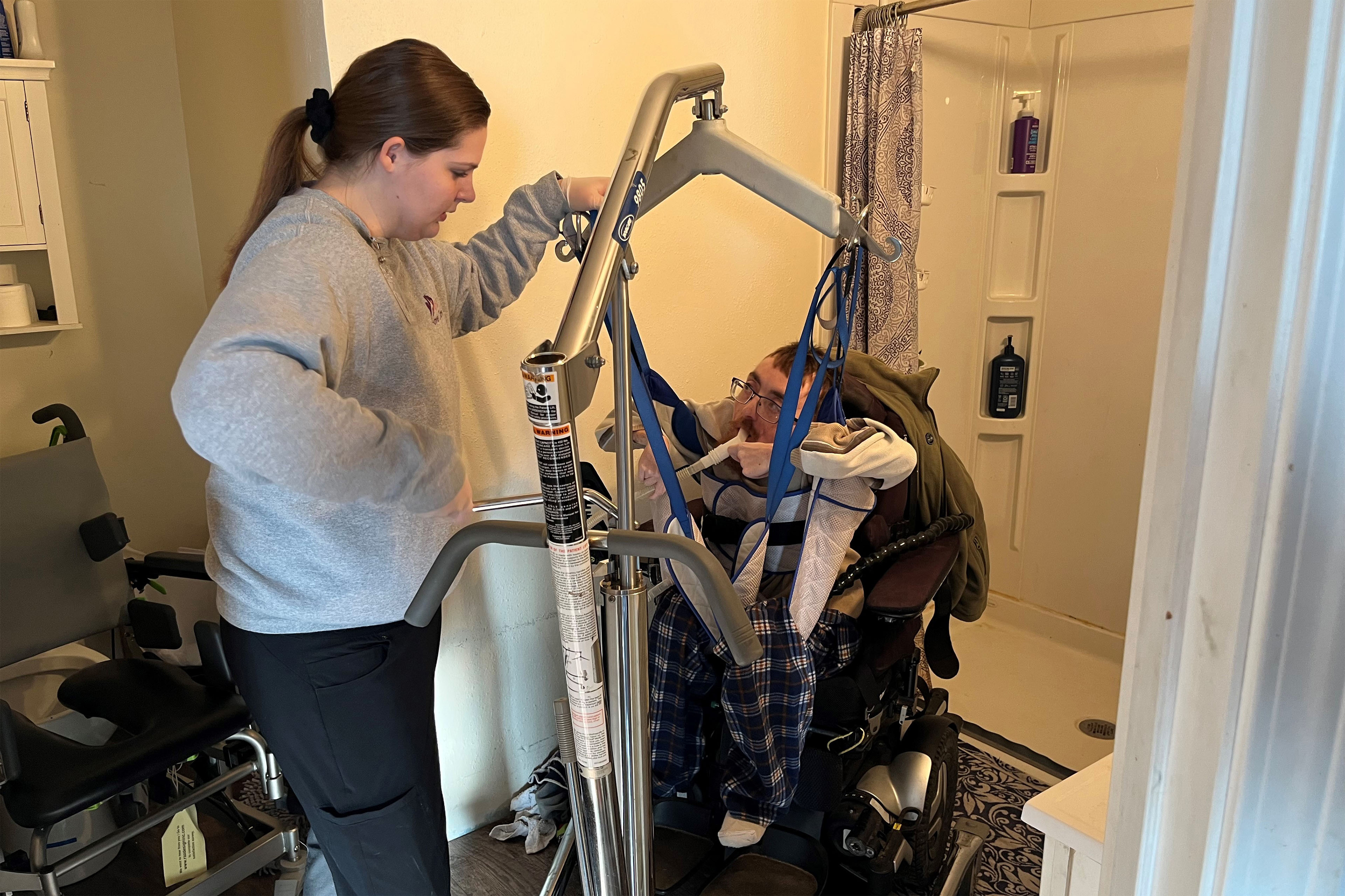 A photo of a health aid lifting a client out of his wheelchair.