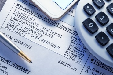 A calculator, smart phone, and a ballpoint pen rest on top of a very expensive medical bill.