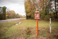 An orange pole and "Warning!" sign along the side of a highway marks the spot where a fiber-optic cable is buried