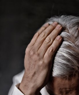 A photo of an older man leaning forward, his hands on his head.