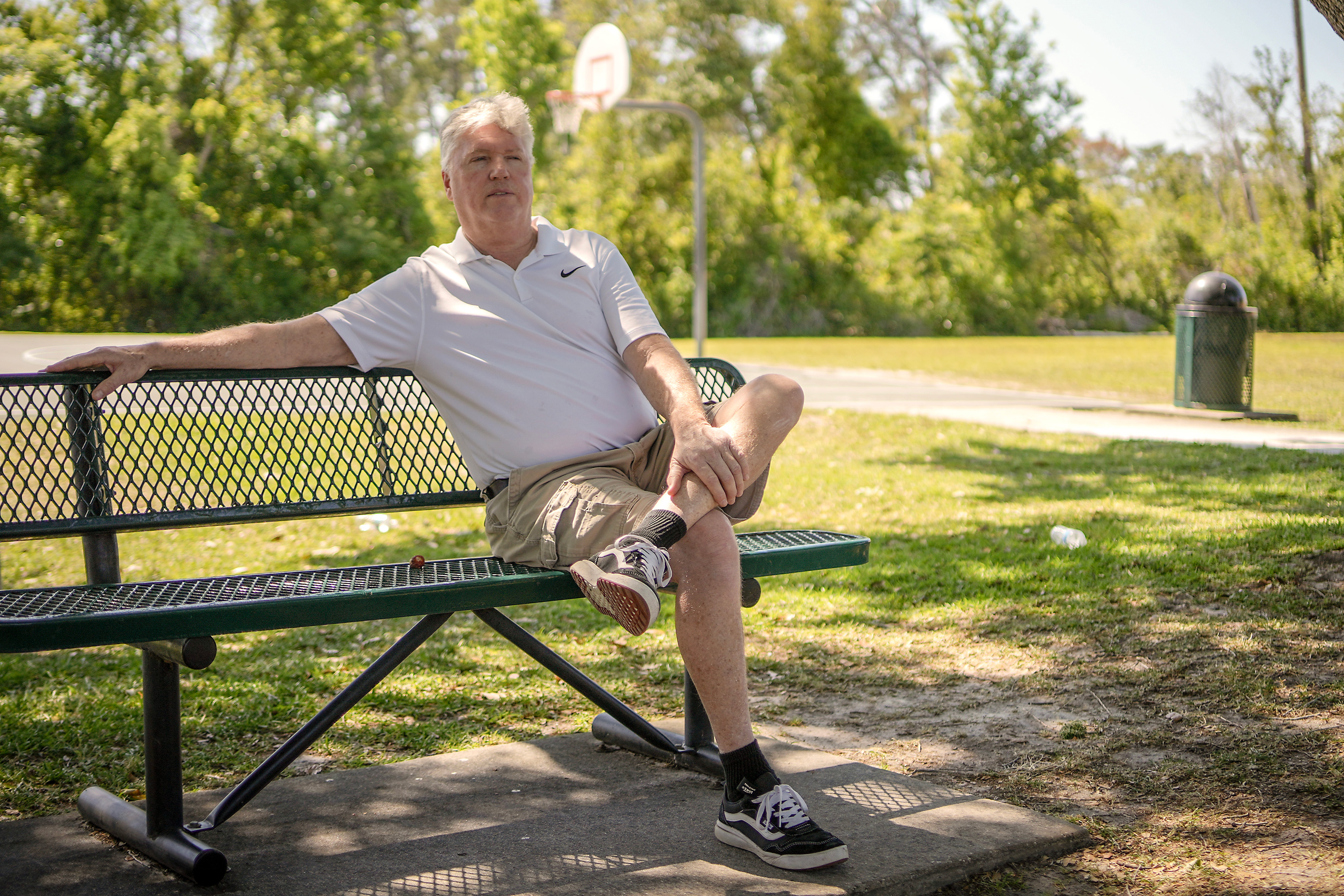 A photo of a man sitting on a park bench outside.