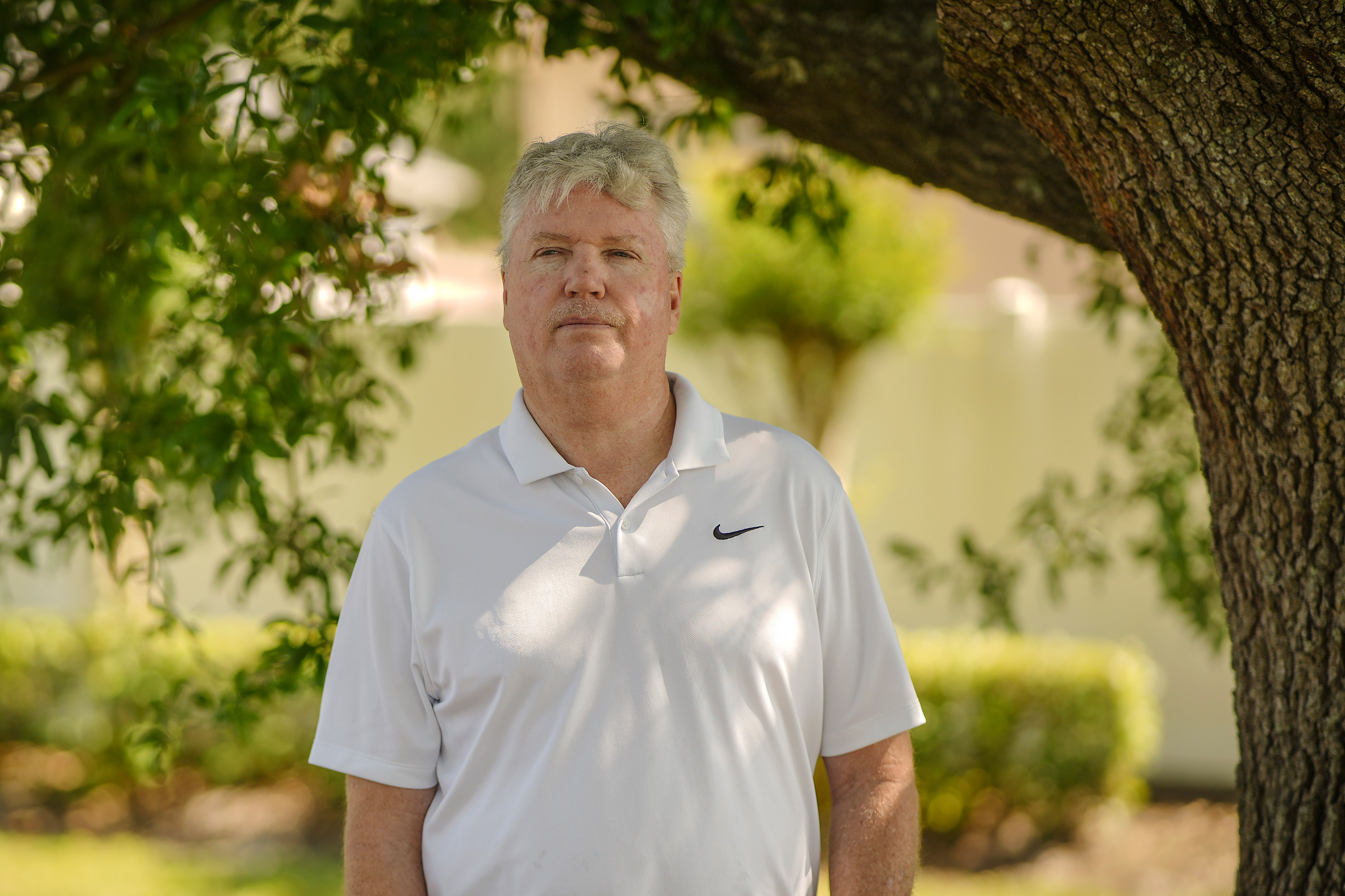 A photo of a man standing for a portrait under a shady tree.