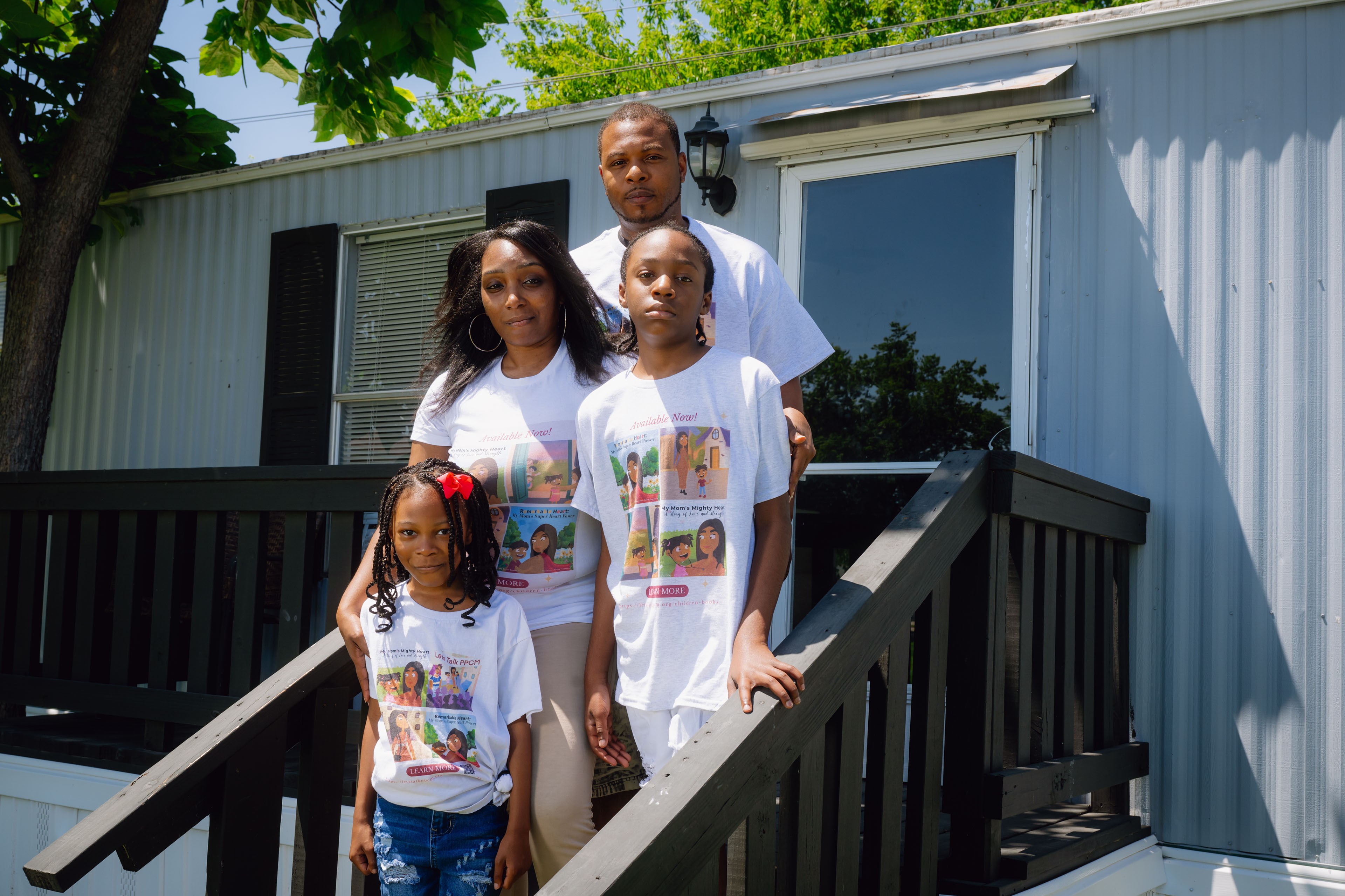 A family portrait taken on the front porch steps of the family's home. The father stands in the back on the highest step. The mother and adolescent son stand below him, with the youngest daughter in the front, on the lowest step.